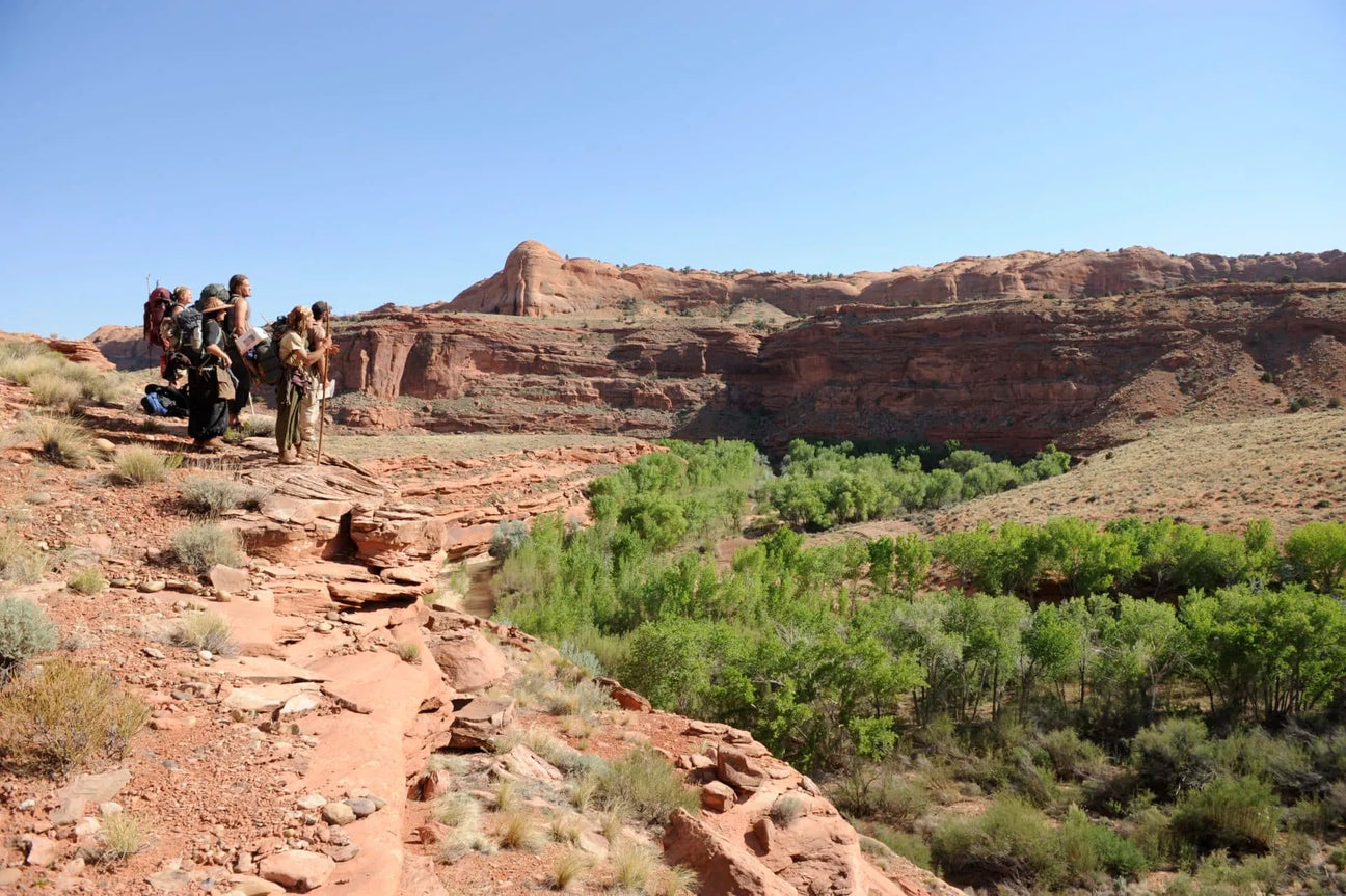 Outdoor survival students stand on the edge of a canyon river looking out to the mountains of the Grand Staircase-Escalante Wilderness.