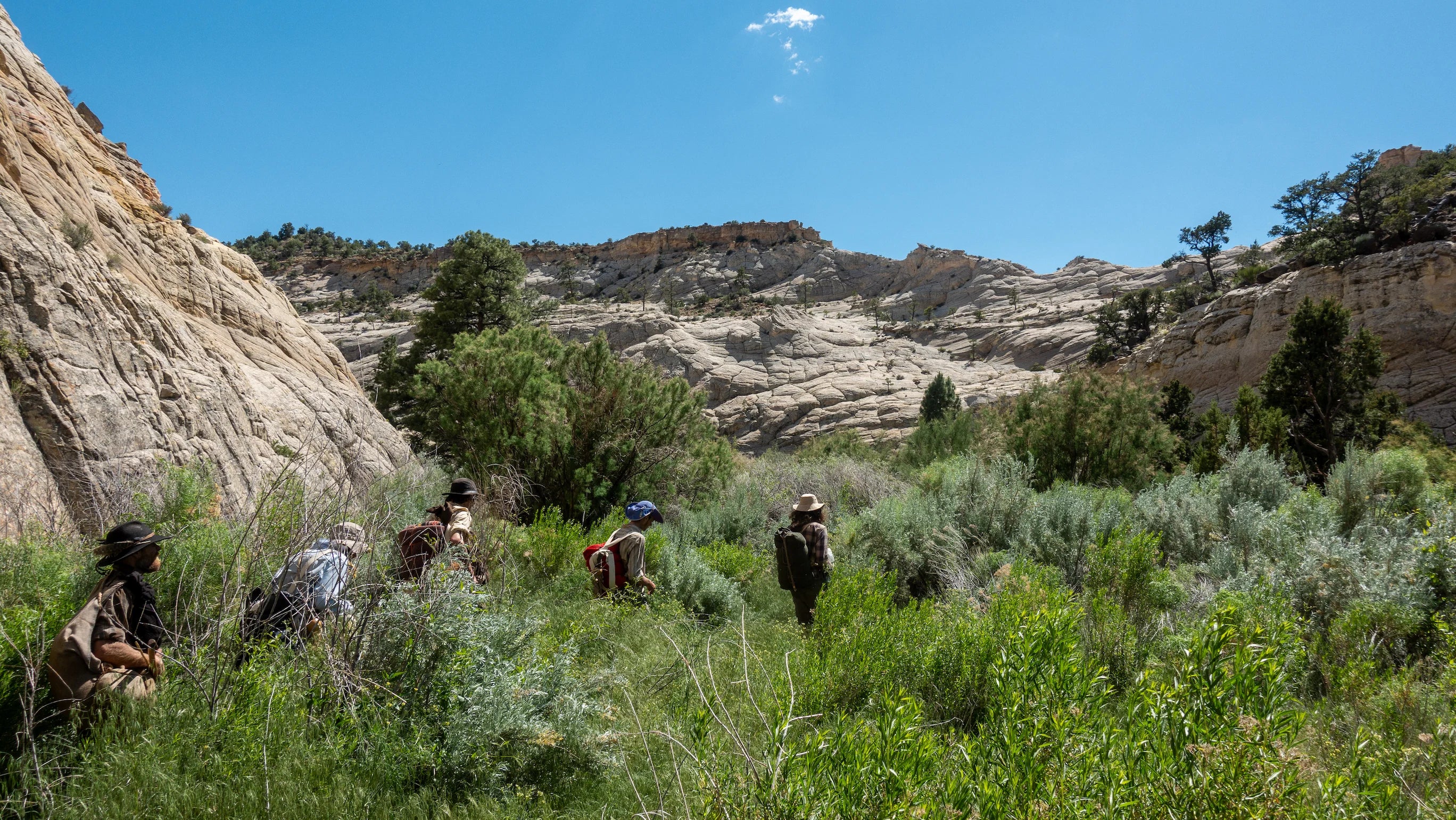 A group of outdoor survival course students hike through the bushes of the Utah wilderness with their primitive survival gear.